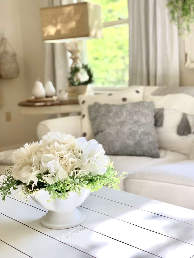 hydrangea on a coffee table. cottage style living room with curtains in the background. 
