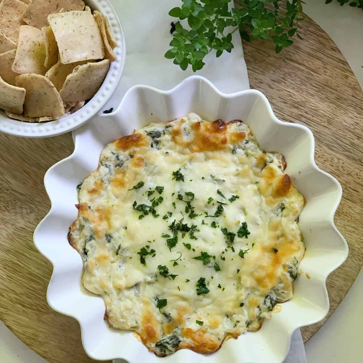 A creamy spinach and artichoke dip made without mayo. This dip sits in a ruffled edge white dish and is served with crackers.