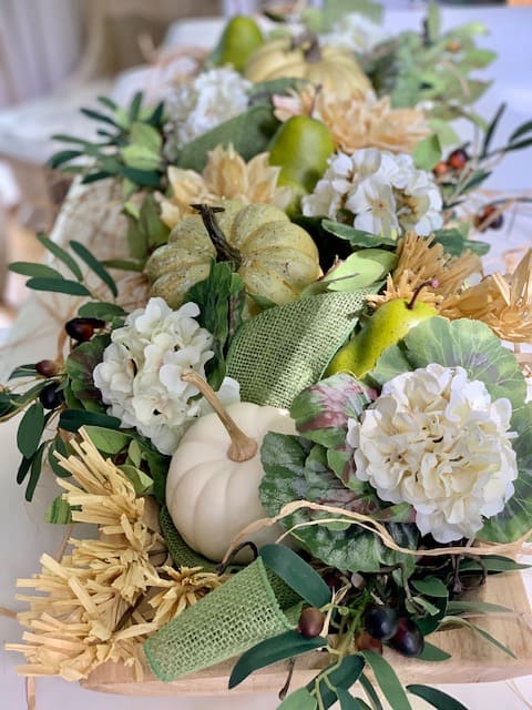 full dough bowl design featuring pears, pumpkins, faux fall flowers, raffia and a wide green burlap ribbon. 