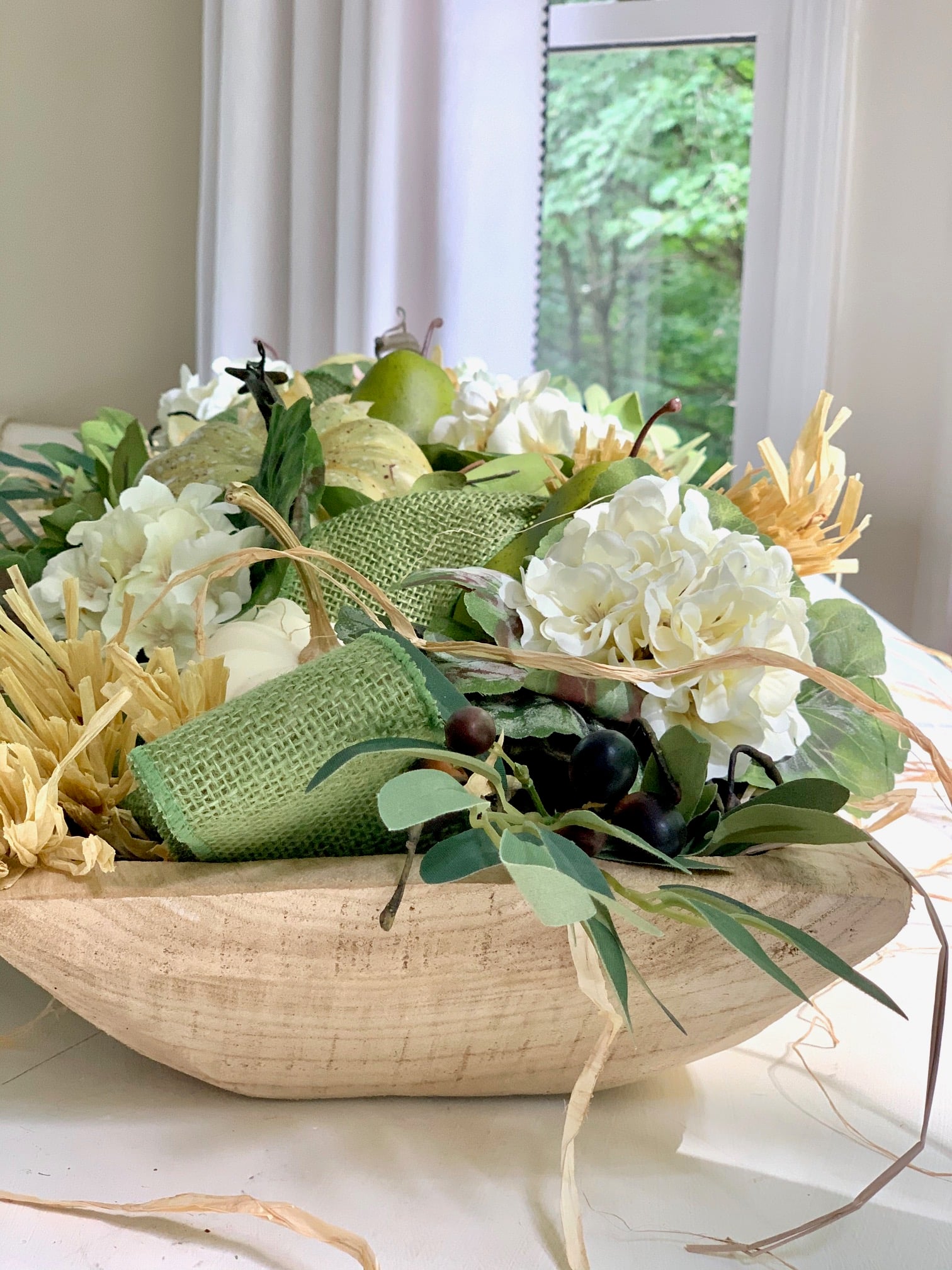 The completed dough bowl. In this image you can see the contents up close. There are olive branches, white blooms and green faux gourds.