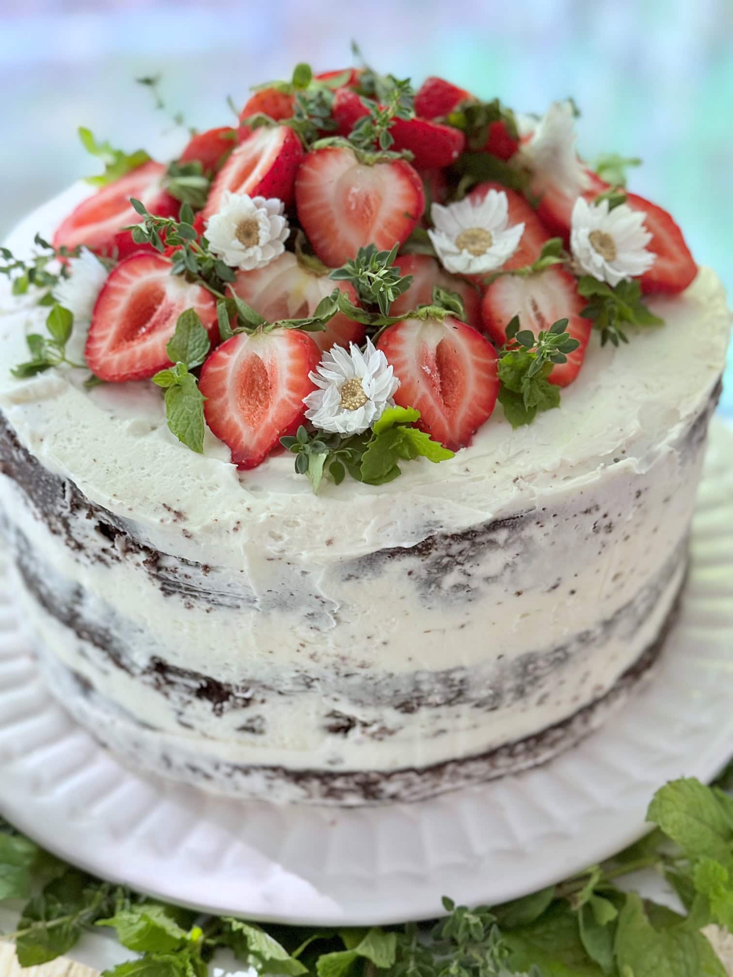 A cake topper with sliced strawberries and little dried daisy like flowers. the greens are herbs. 