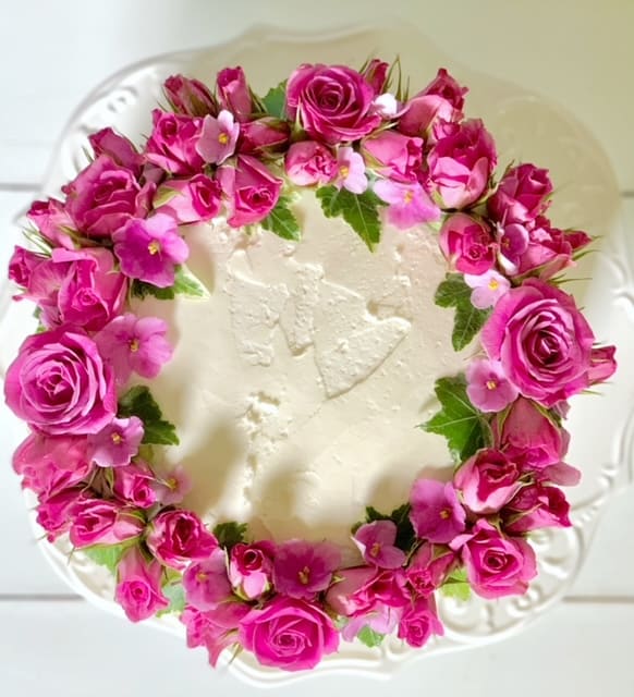 top view of cake decorated with roses, ivy and african violet flowers