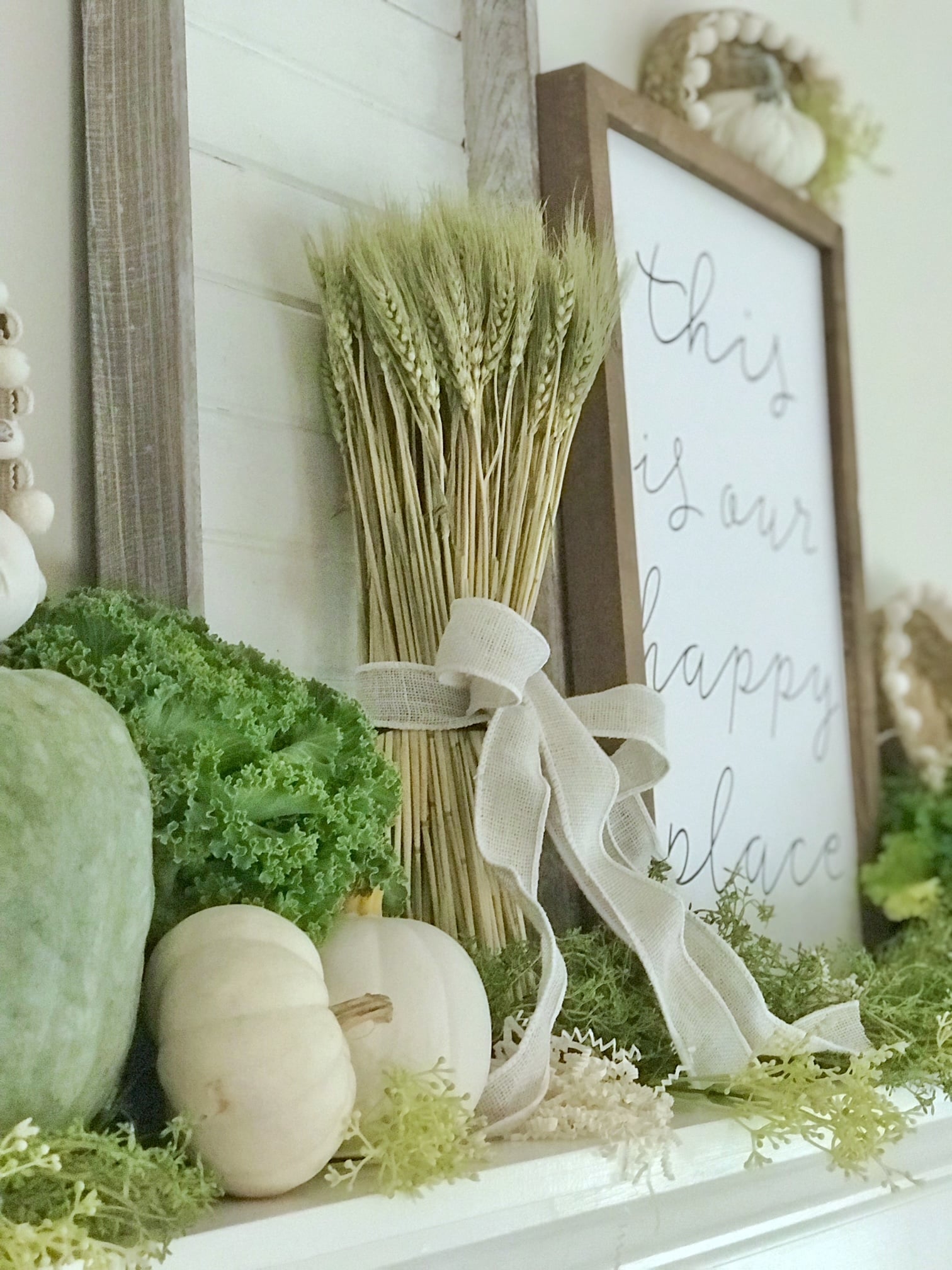 A mantel with a bundle of wheat and other fall green and white decor.