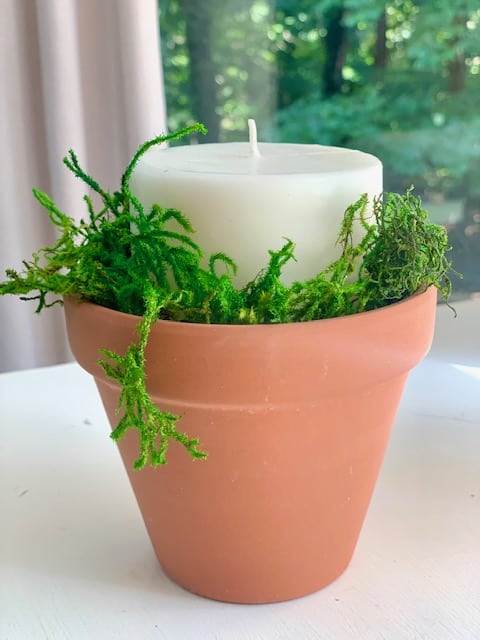 clay pot with moss and a pillar candle.