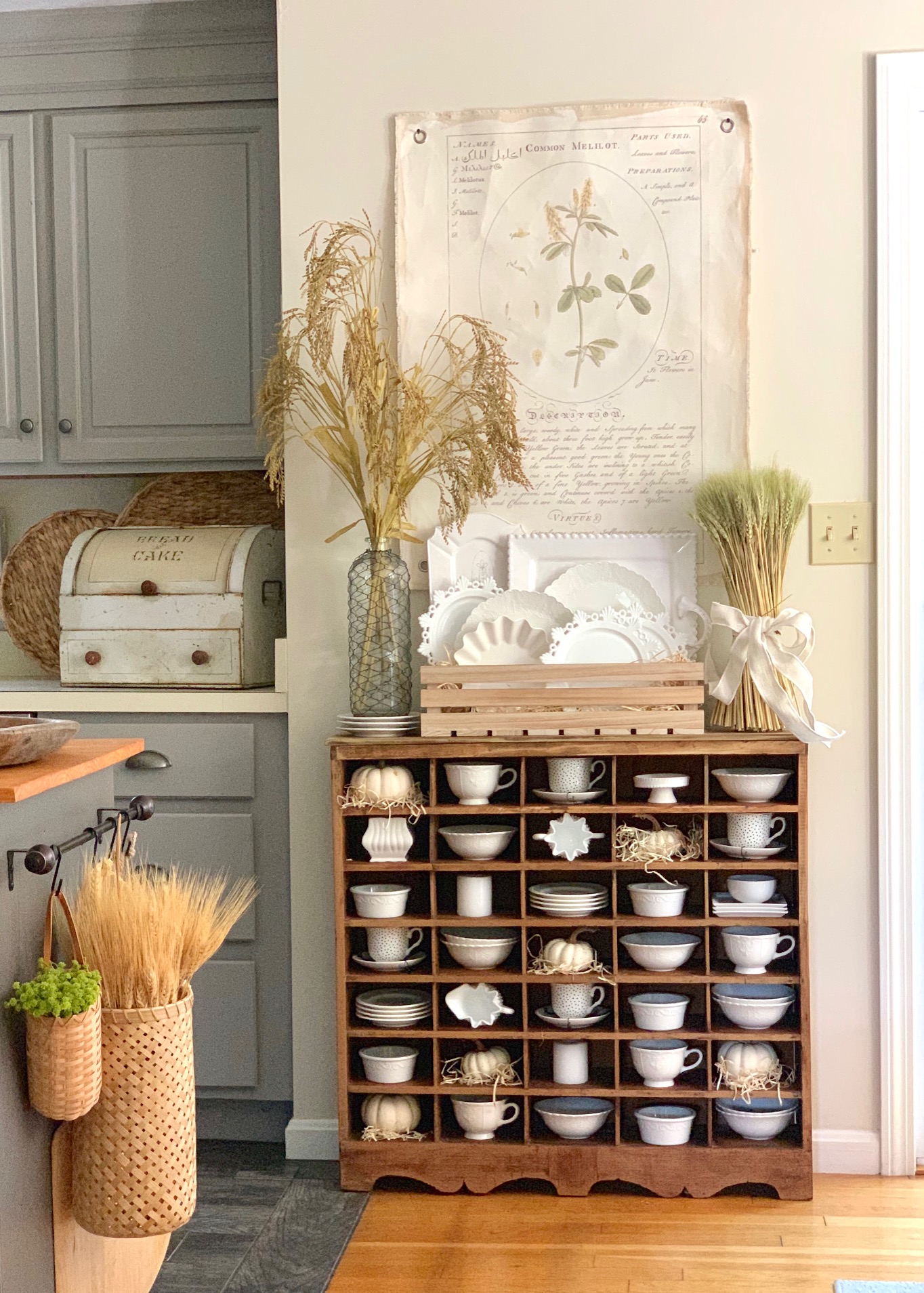A bundle of wheat on a antique cubby with dishes.