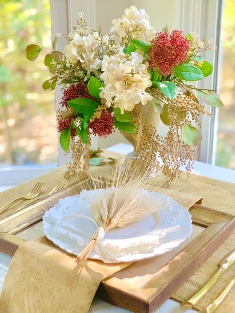a small bundle of wheat wrapped in ribbon on a place setting. 