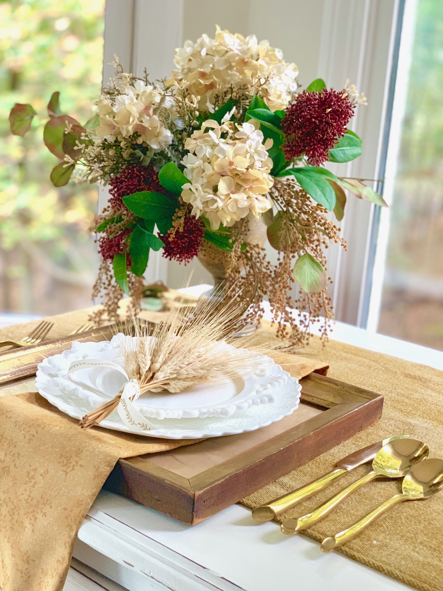 A faux flower arrangement behind a table setting where there are little wheat bundles on the plate.