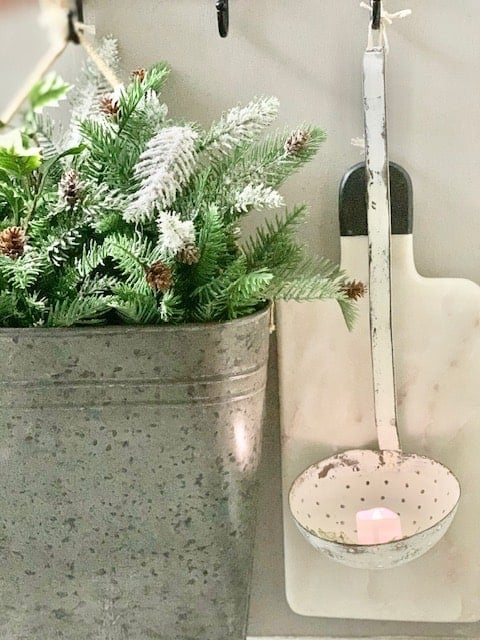 The end cap of our kitchen island with a marble cutting board, vintage soup spoon and a tin bucket of Christmas greens