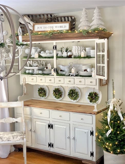 A Dining room hutch decorated for Christmas with green and white decor.