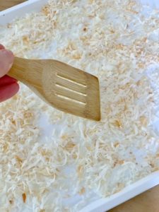 using a spatula to stir coconut on the baking sheet