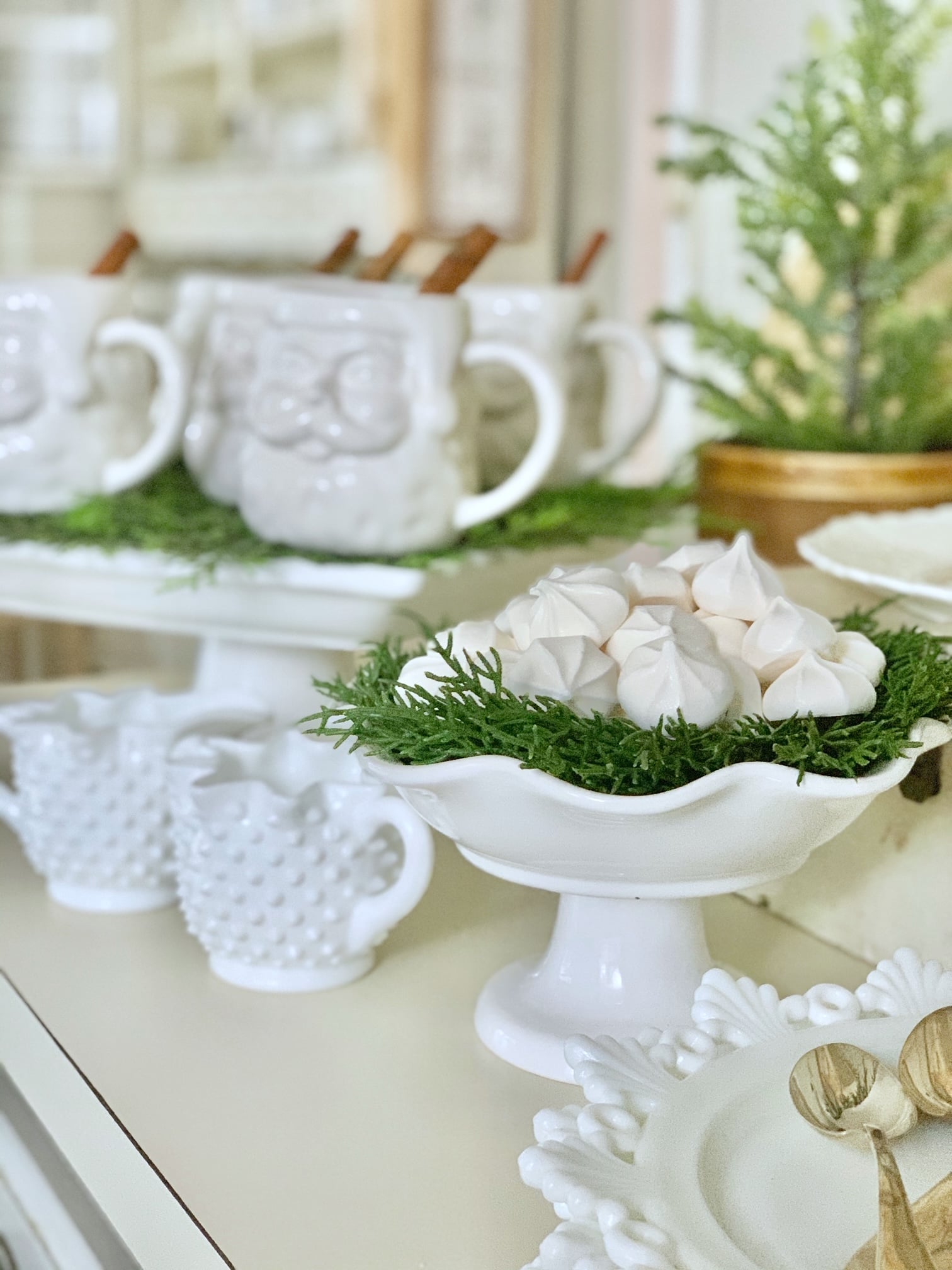 White santa mugs on a cake stand with a cinnamon stick in it with cookies and other delights on our kitchen counter. 