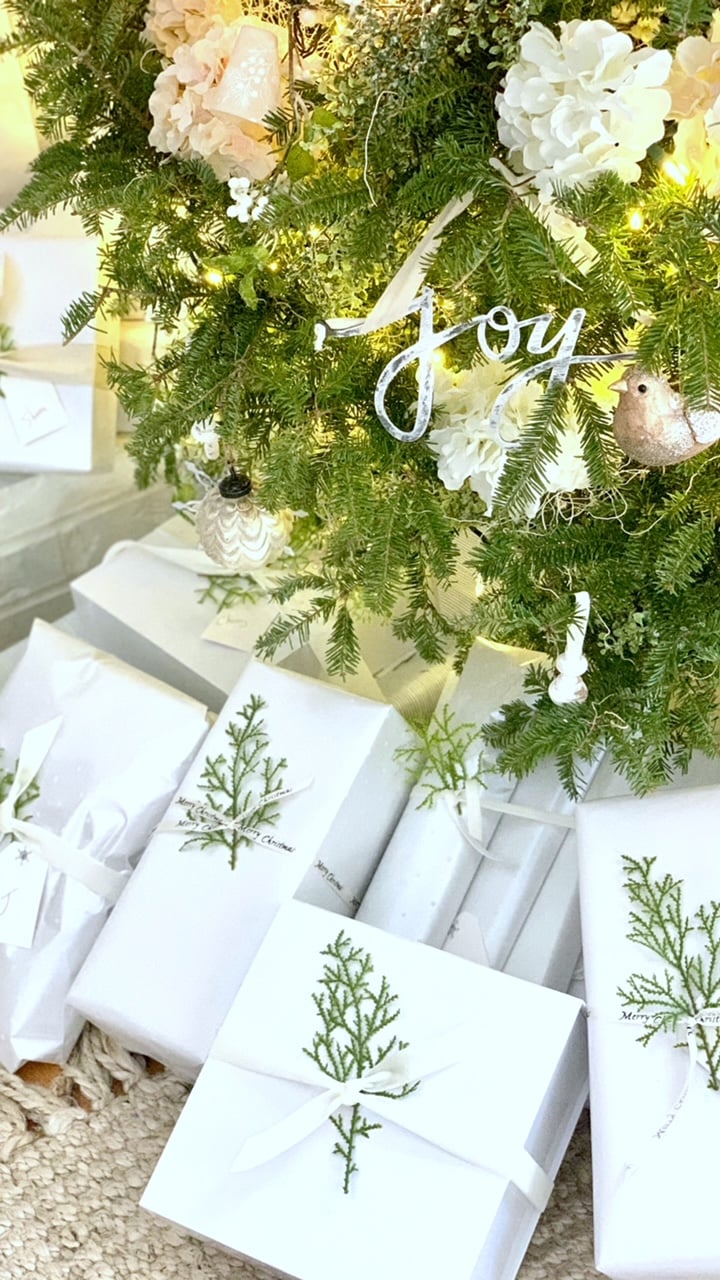 White wrapped presents with a sprig of cedar under the bow. All placed under a tree. 