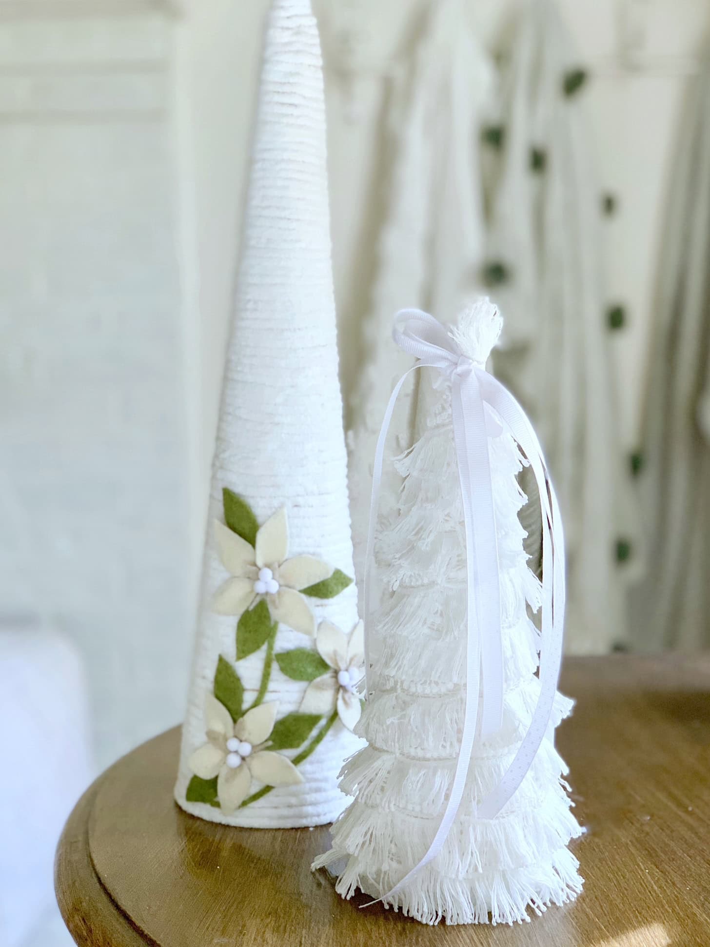 Two white yarn wrapped Christmas trees. One with a bow on top the other with felt poinsettias.