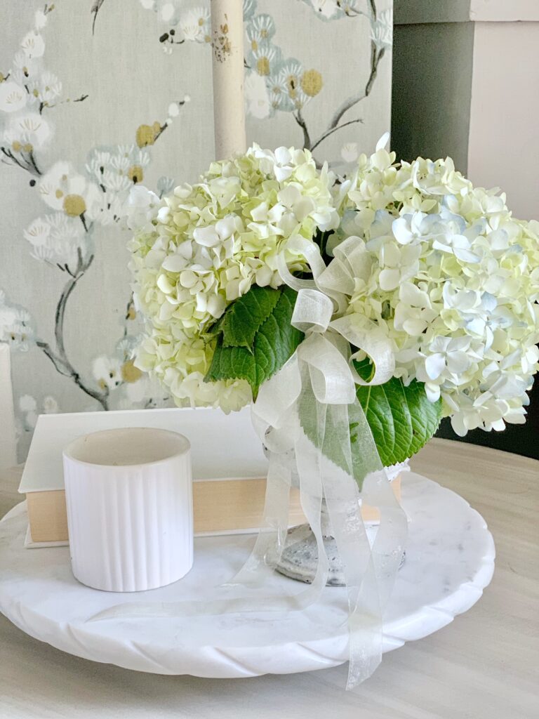 compote vase with fresh white hydrandea and a bow on a side table