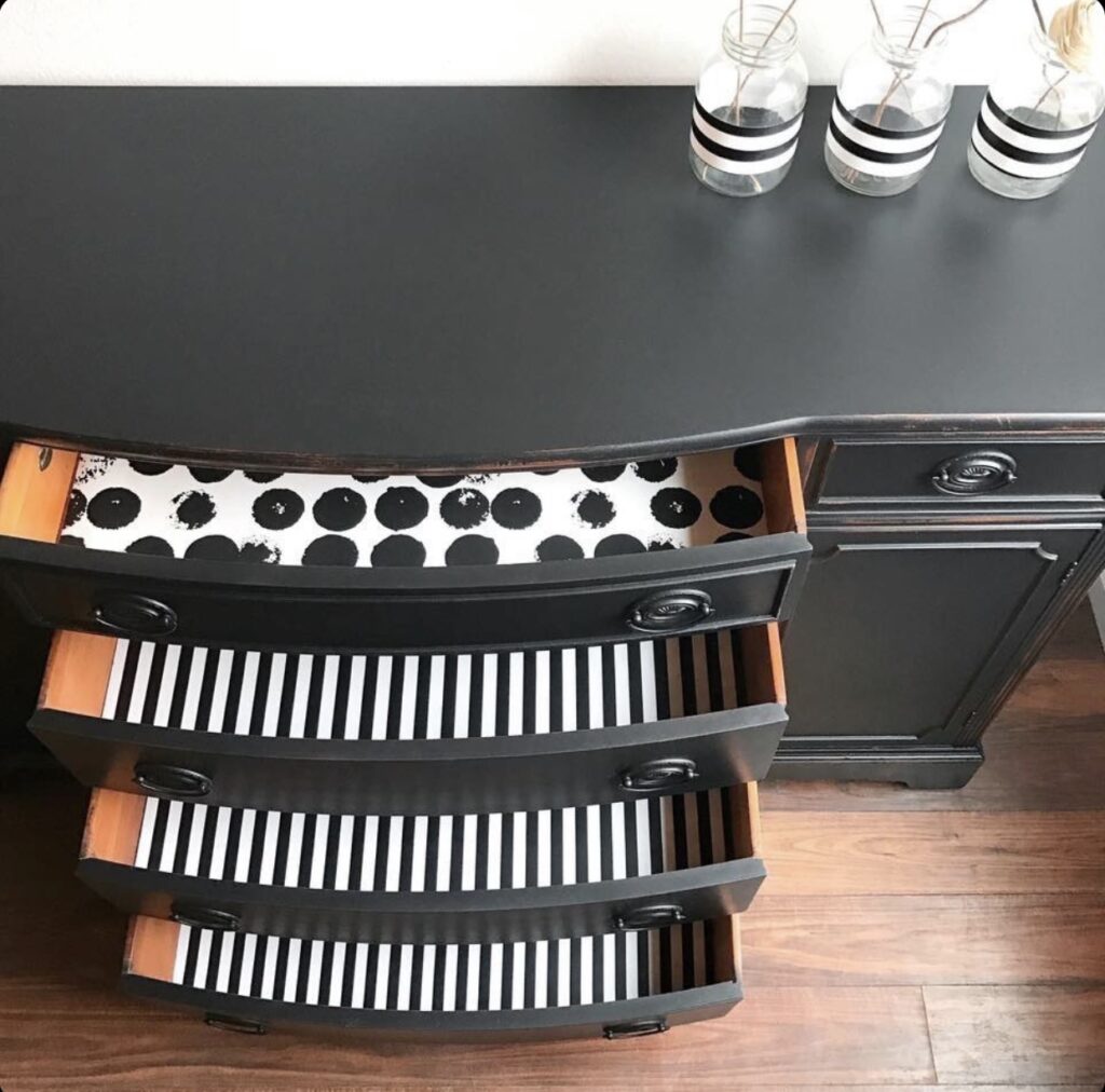 A top view of a black dresser with the drawer open showing black and white stripped drawer liners. 
