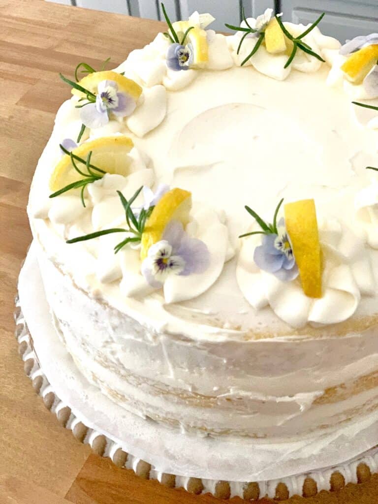 lemon cake decorated with violets, lemon wedges and rosemary sprigs. 