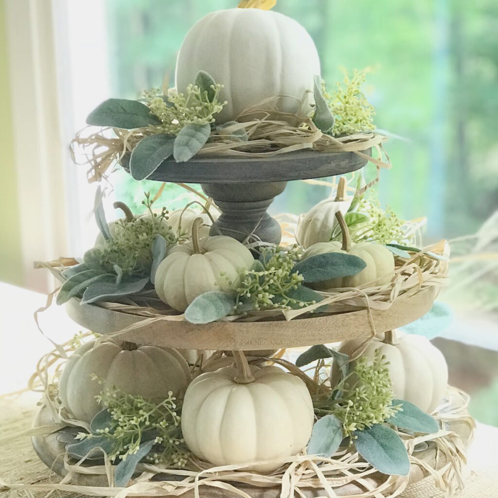 Stacked tiered tray, fall floral centerpiece using faux greens, mini white pumpkins and raffia. The trays are all footed pedestal style stacked on top of one another.