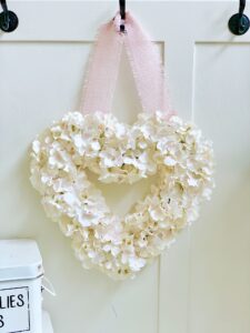 finished project. sift cream hydrangea with hints of pink on a heart shaped wreath with a pink ribbon for hanging.