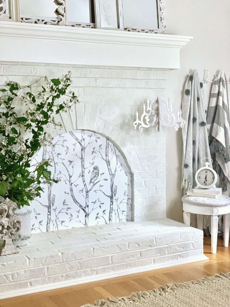 white painted fireplace with my diy fireplace screen and some decorative items on the hearth and next to the fireplace. 