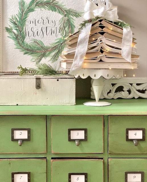 same open book stack on a green apothecary with decor items. 