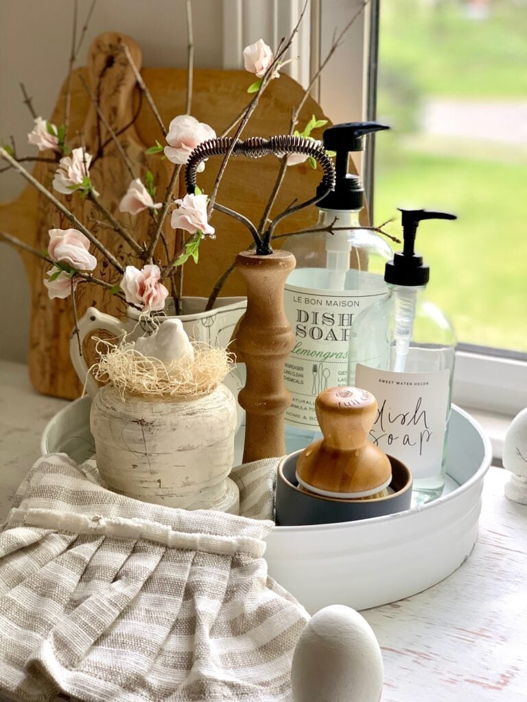 a kitchen sink tray hold diy cherry blossom branches, dish soap dispensers and a scrub brush. 