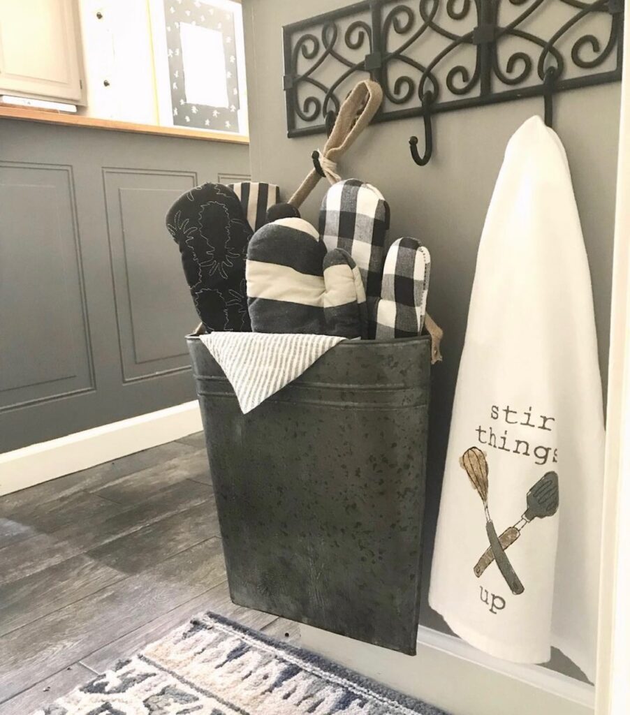 end cap with a metal wall pocket of oven mits with a tea towel hanging from a black scroll coat rack. 