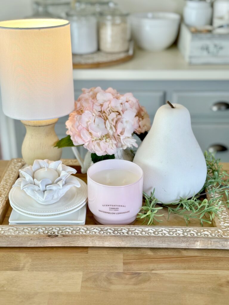a tray with a diy cordless lamp with a large white pear. a small pitcher of hydrangea, a candle and some stacked plates. 