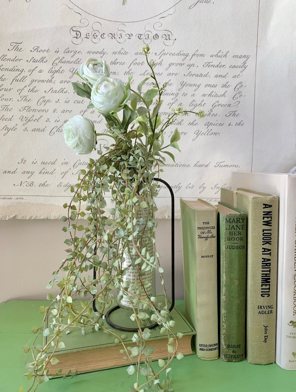 a vase of faux green and white flowers next to books that are also green and white