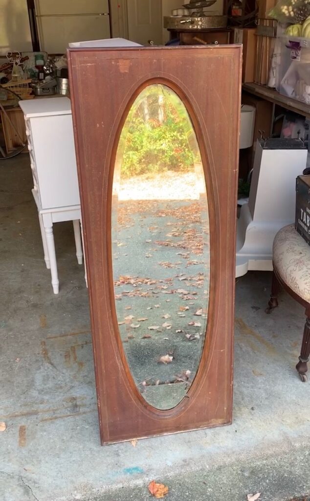 antique mirror with heavy wood frame that is dark stain. The mirror is oval shaped. 