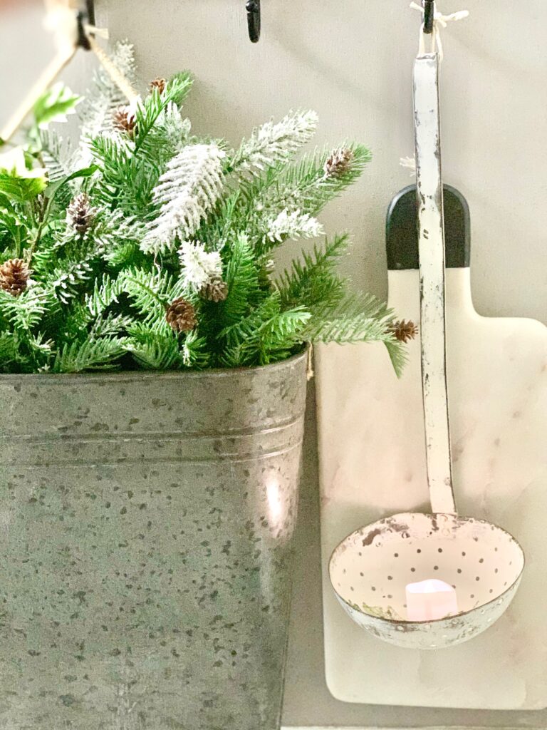 end cap with hanging metal bucket with Christmas greens and a vintage ladle with a votive candle. 