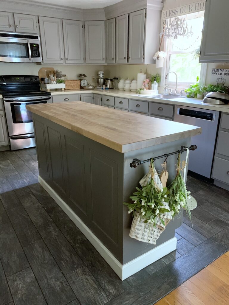 our kitchen island with a small curtain rod with towel, greens, cutting board hanging. 