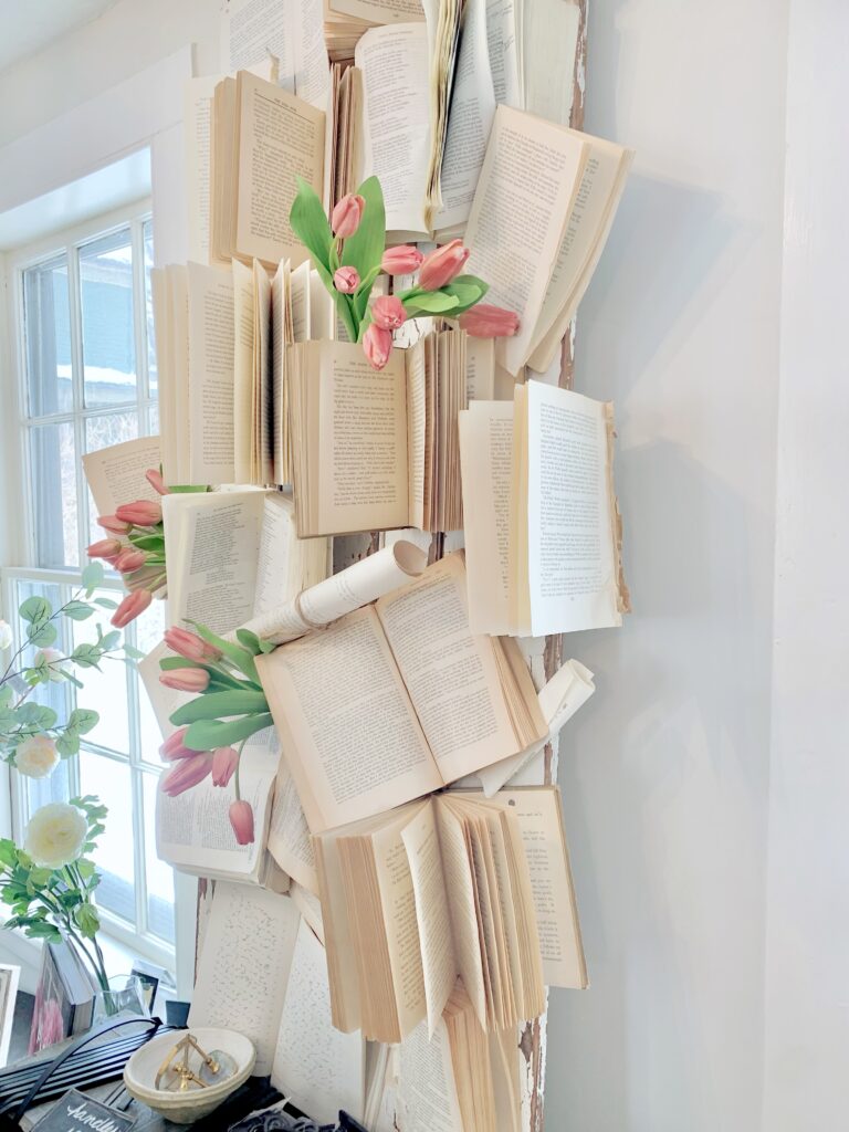 a Wall with books attached in a climbing manor. there are bunches of pink tulips tucked in. 