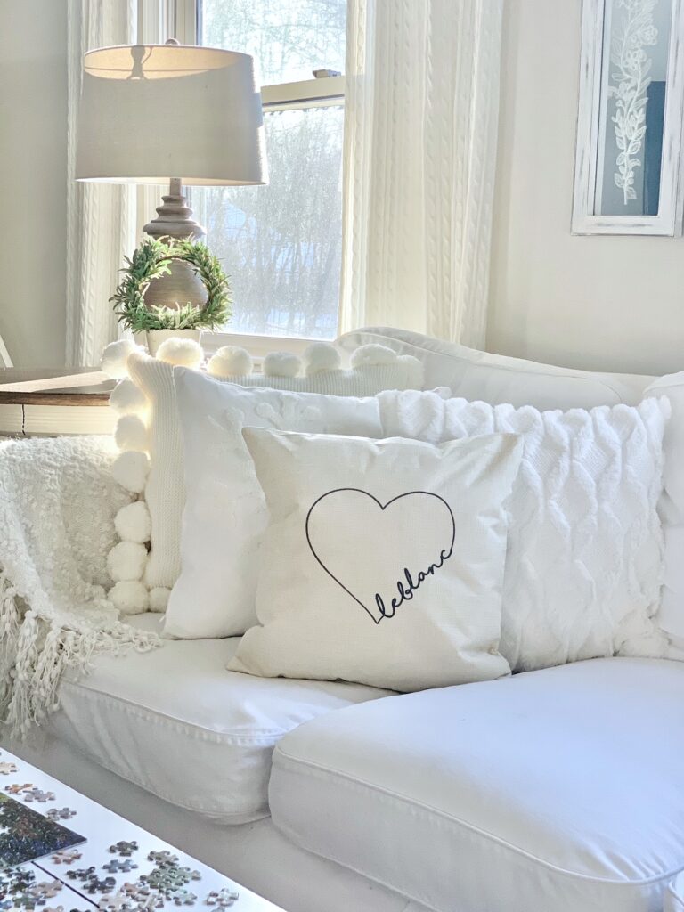 white slipcovered couch, throw pillow, table and lamp. 