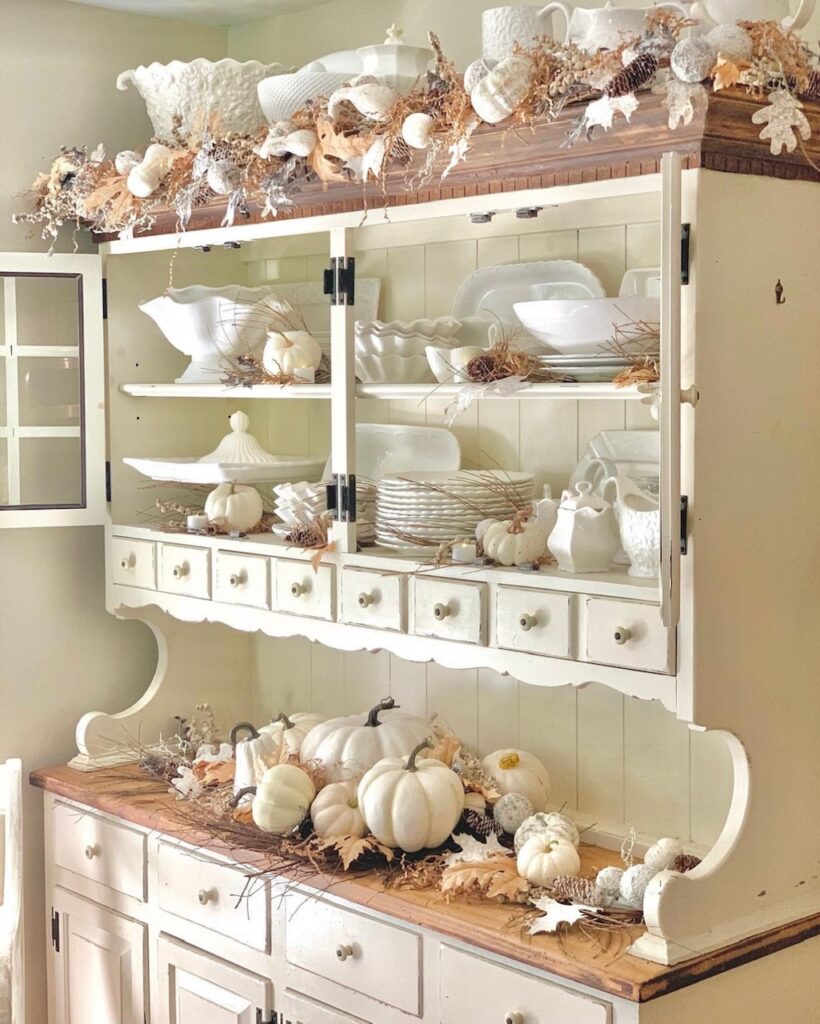 The cabinet decorated for fall with pumpkins and fall leaves. 