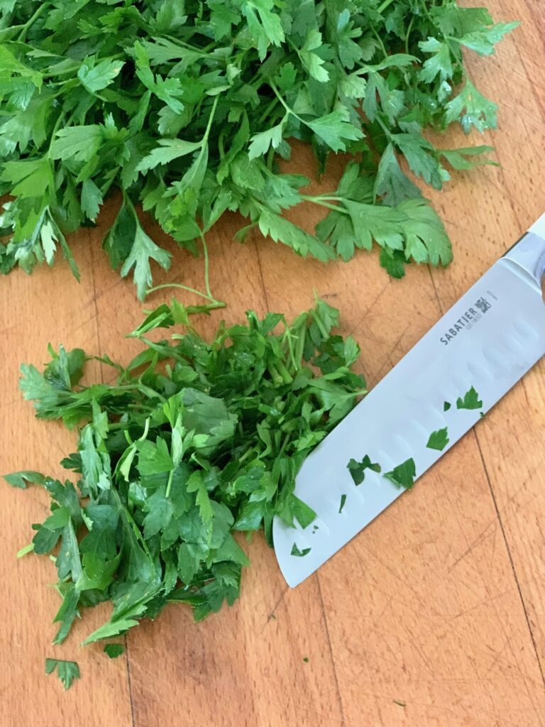 parsley on a cutting board with a knife. 