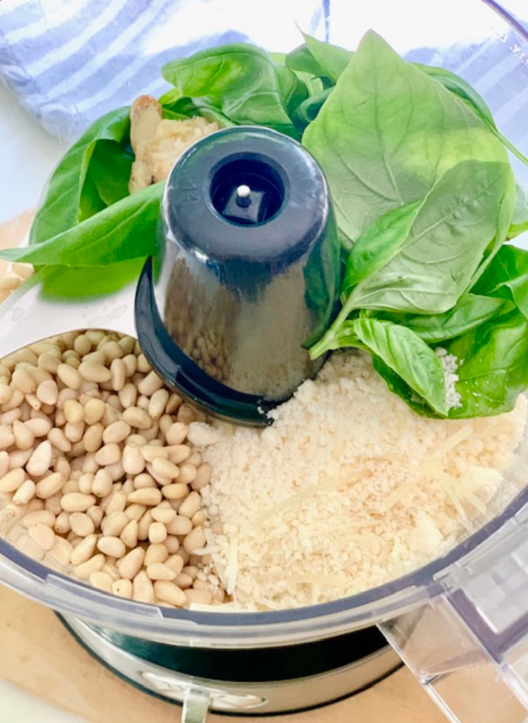 A food processor with the ingredients for pesto, including fresh basil. 