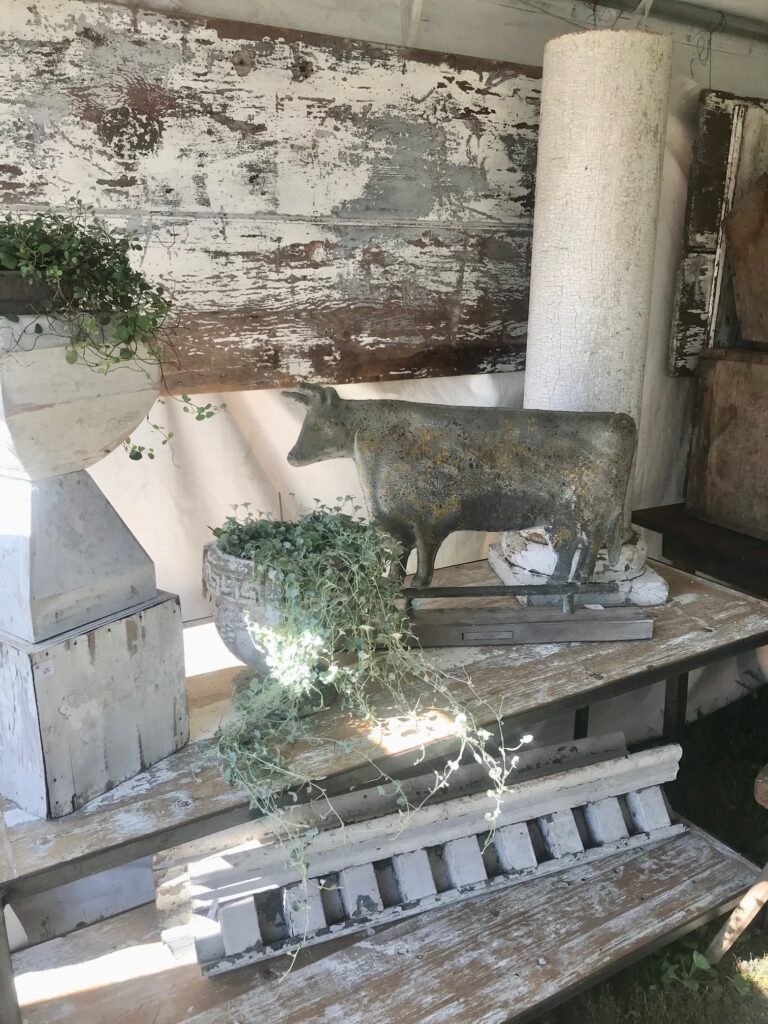 A booth at brimfield with fabulous chippy table and columns with a decorative cow and planter. 