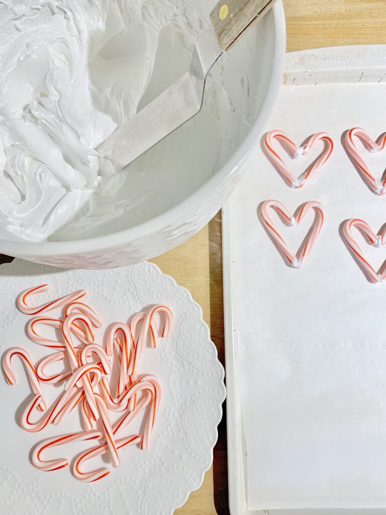 a large white mixing bowl with meringue frosting. a white plate with mini candy canes and candy cane hearts on a cookie sheet.