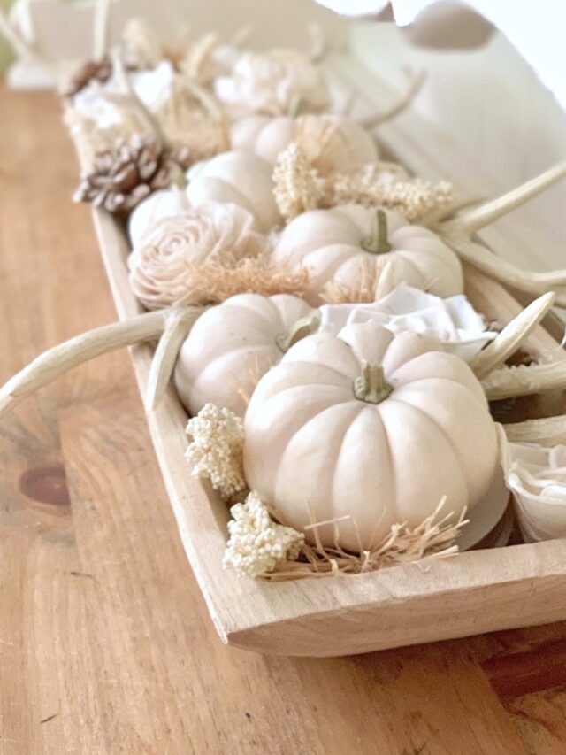 a dough bowl with white mini pumpkins, antlers, sola flowers, pinecone and raffia.