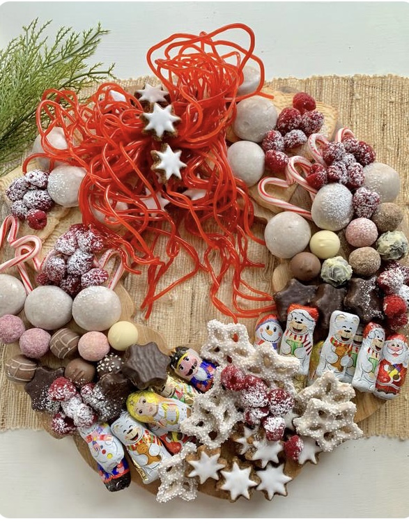 A wreath shaped charcuterie board covered with Christmas cookie and candy. on the top of the wreath is a bow made from string licorice. 