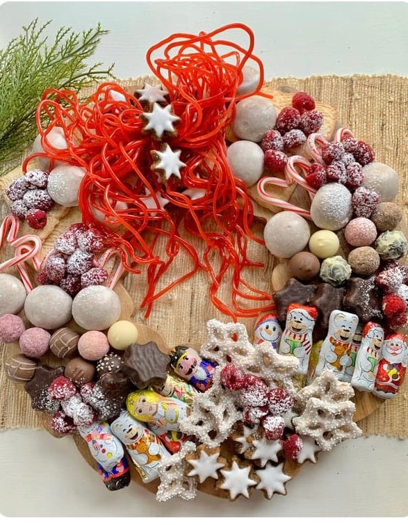 A wreath shaped charcuterie board covered with Christmas cookie and candy. on the top of the wreath is a bow made from string licorice. 