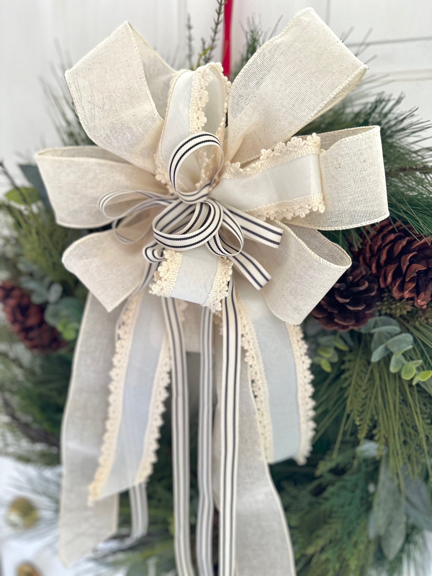Large pine wreath with a large over the top cream colored bow that is made from 3 different ribbons.