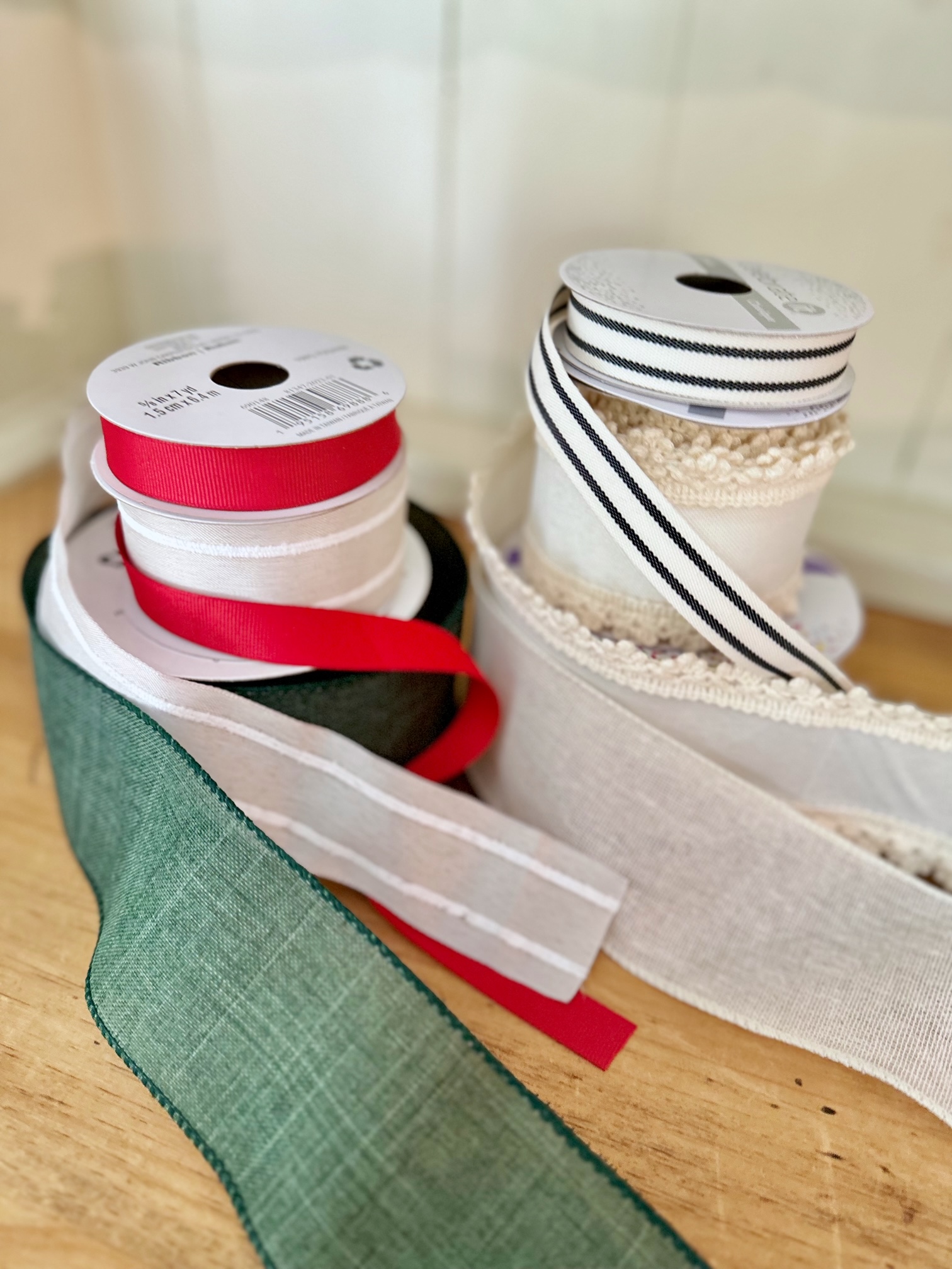 2 stacks of ribbon that coordinate with one another. the first stack has green, cream and red. the second are all off white but different sizes and textures.