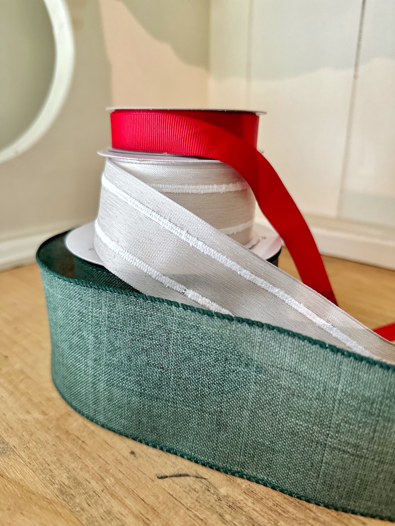 A stack of green wired ribbon, cream colored wired ribbon and red that is not wired.