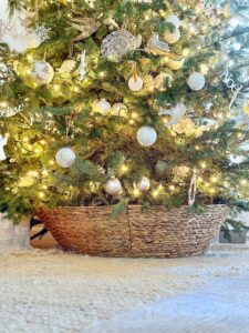 the tree collar with the wide opening on top under a fresh Christmas tree that is decorated in white and gold.