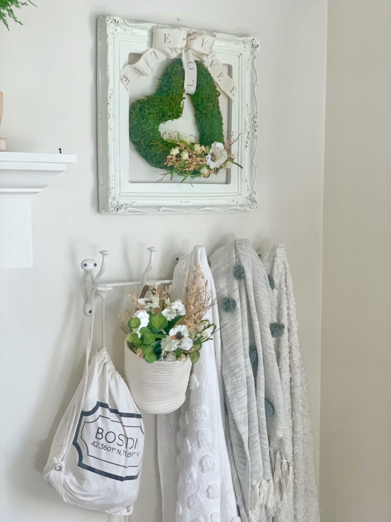 The wreath and frame on the wall. there is a coat rack below with throw blankets hanging.