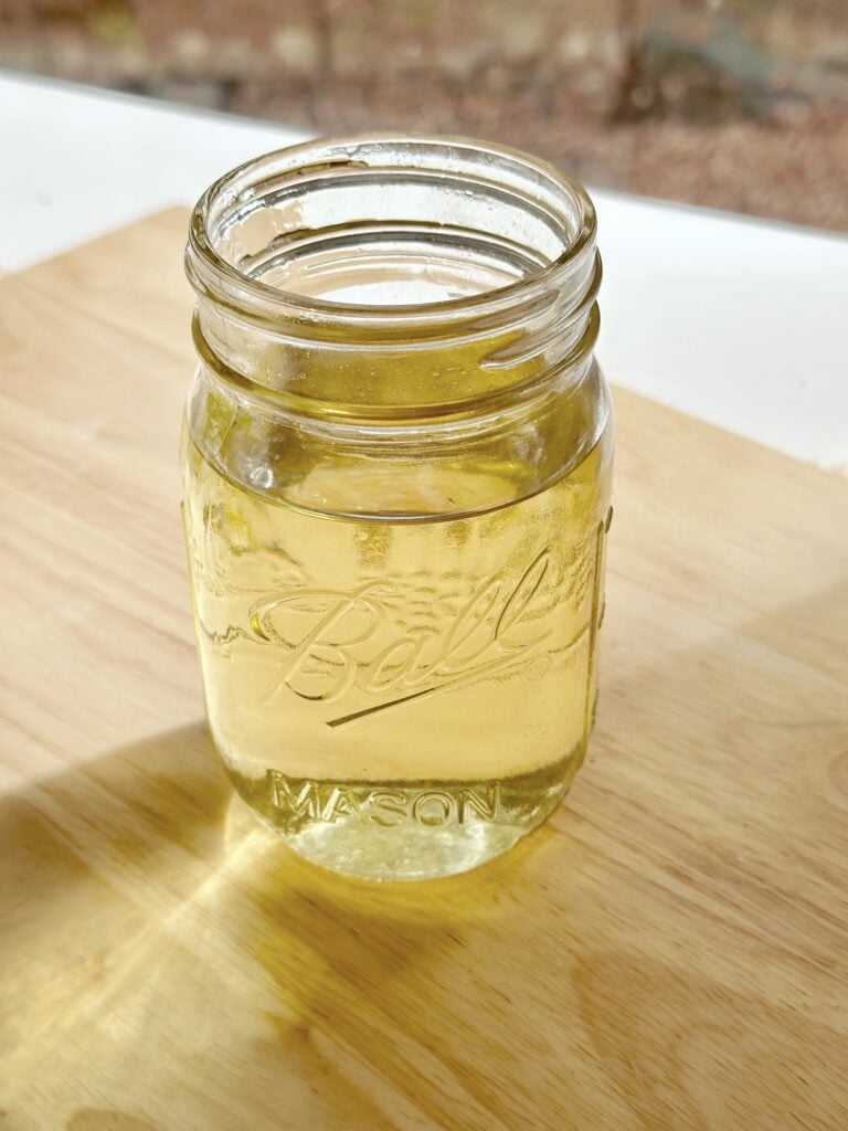 The jar out of the crockpot with the wax melted. the wax has an amber tone while melted but will dry white. 