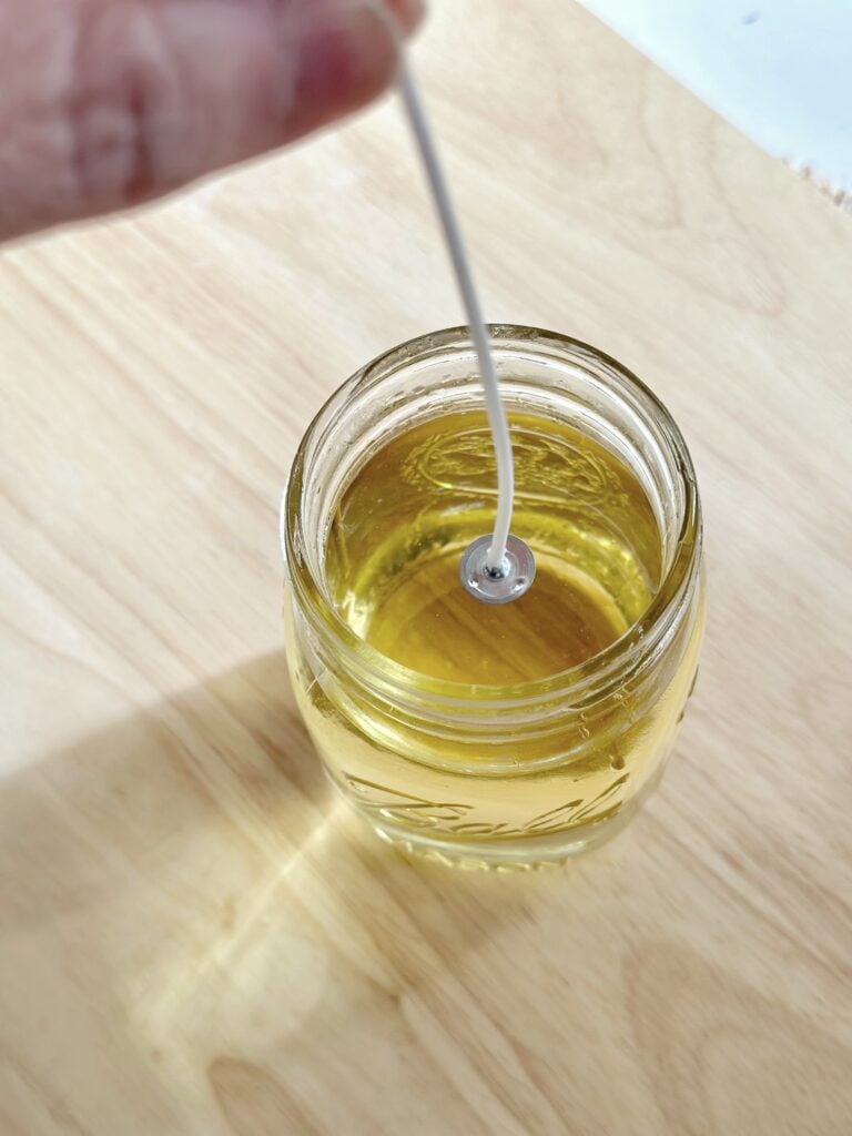 Placing the wick in the the jar of melted wax. 