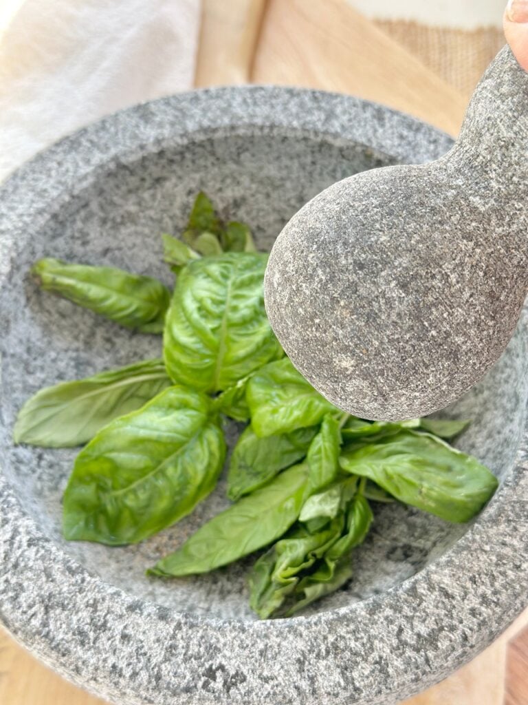 Showing basil leaves in a mortar and pestle ready to be ground. 