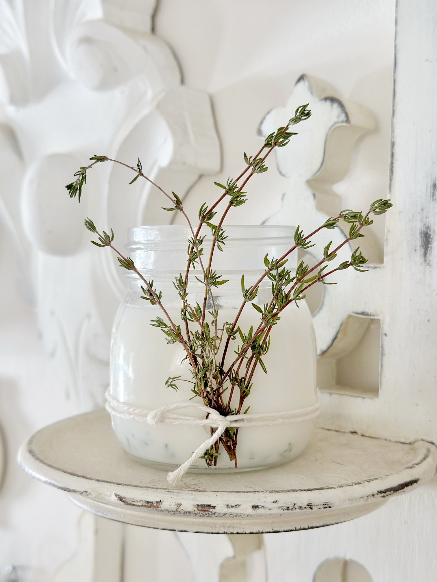 A close up of the finished candle. There are sprigs of thyme shooting up the front tied with twine. 